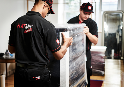 FlatRate movers carry a plastic wrapped piece of furniture